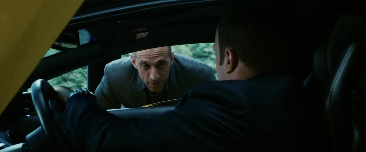 Zookeeper (2011) movie still: medium — An exterior view looking into the cabin of a high-performance sports car. A man in a suit leans down to talk…