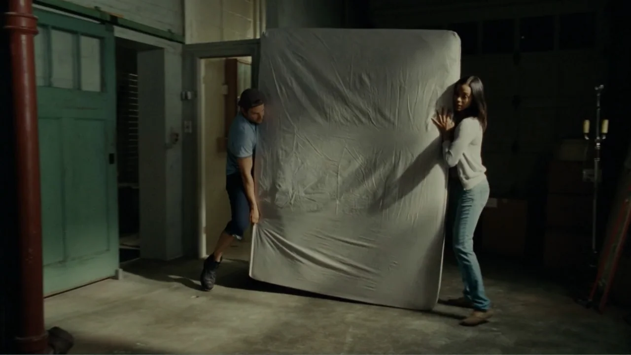The Words (2012) movie still: fullbody — A dimly lit residential garage with a painted green sliding door and concrete floors. A man and a woman…