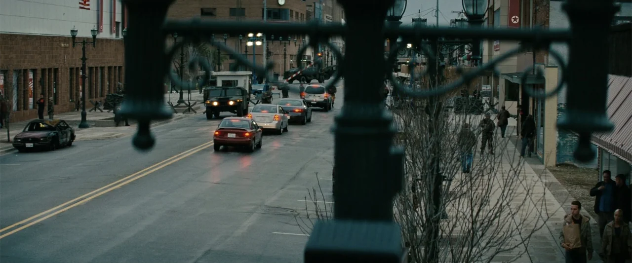 Red Dawn (2012) movie still: wide — An urban thoroughfare features a military checkpoint with soldiers and a humvee present. Civilian cars wait in a…