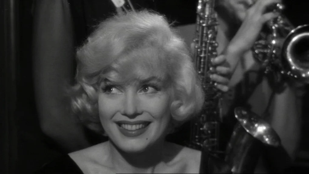 Some Like It Hot (1959) movie still: closeup — A dimly lit indoor musical performance area with musicians playing brass instruments in background. A…