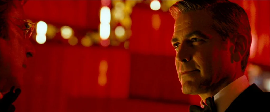 Ocean’s Thirteen (2007) movie still: medium — Two men face each other inside a dimly lit casino with red wall decor. One man in a tuxedo is visible…