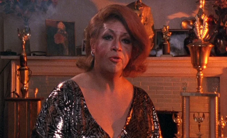 Paris Is Burning (1990) movie still: medium — A woman stands in front of a fireplace mantel decorated with numerous award trophies. She faces the…