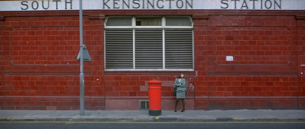 The Crying Game (1992) movie still: wide — The red tiled exterior wall of South Kensington Station features a large barred window. A woman stands on…