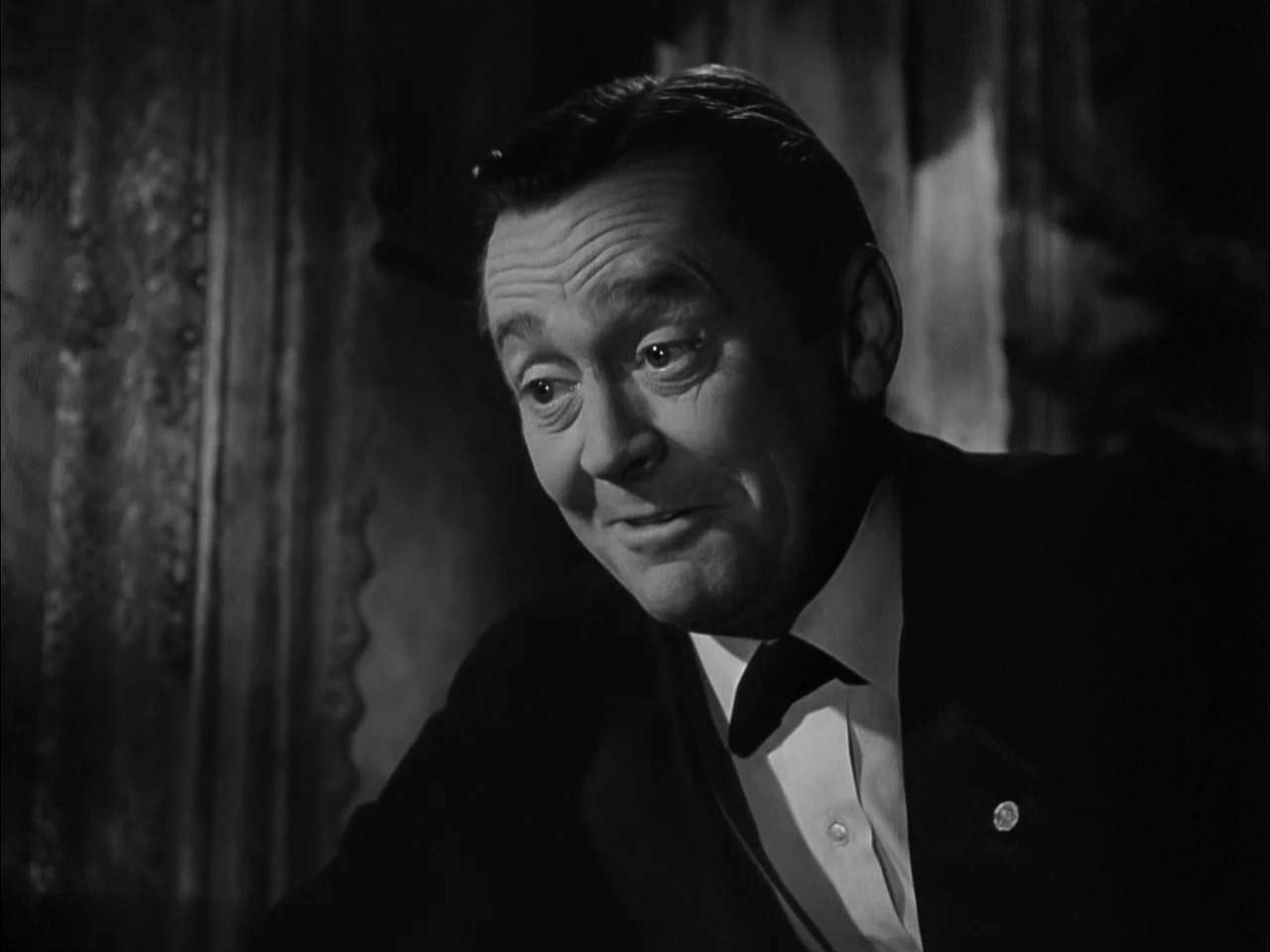 A Tree Grows In Brooklyn (1945) movie still: closeup — A dimly lit room features heavy, dark curtains forming a textured backdrop. A man in formal…