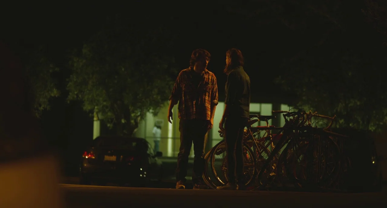Short Term 12 (2013) movie still: fullbody — A man and a woman stand by bicycle racks in a dark parking lot. An amber streetlamp illuminates them…