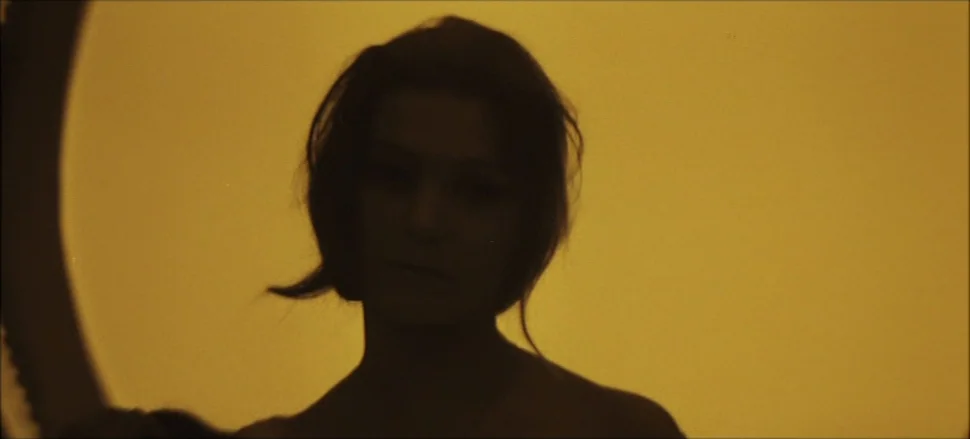 Solaris (1972) movie still: closeup — An interior space with a solid, vibrant yellow backdrop. A woman stands centered in the frame as a silhouette.
