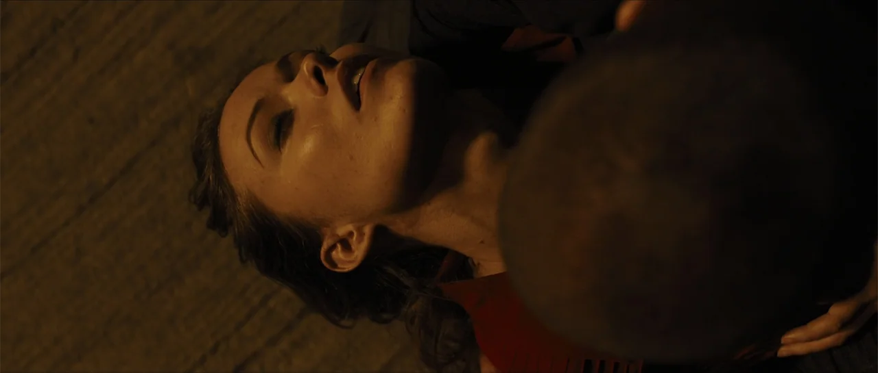In Time (2011) movie still: closeup — A dark, textured asphalt surface at night serves as the setting for the shot. A man leans over a woman who…