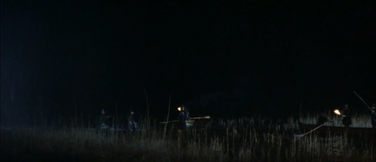 Ludwig (1973) movie still: wide — Dark marshland at night with tall reeds silhouetted against a black sky. Several figures in small wooden boats…