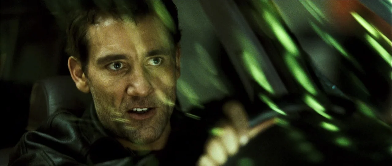 Shoot 'Em Up (2007) movie still: closeup — A dark, cramped space inside a moving vehicle at night with green light reflections. A man with stubble…