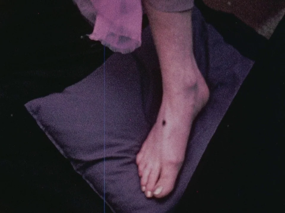 The Wormwood Star (1956) movie still: closeup — A bare foot rests on a dark pillow set against a black background. The foot is angled slightly…