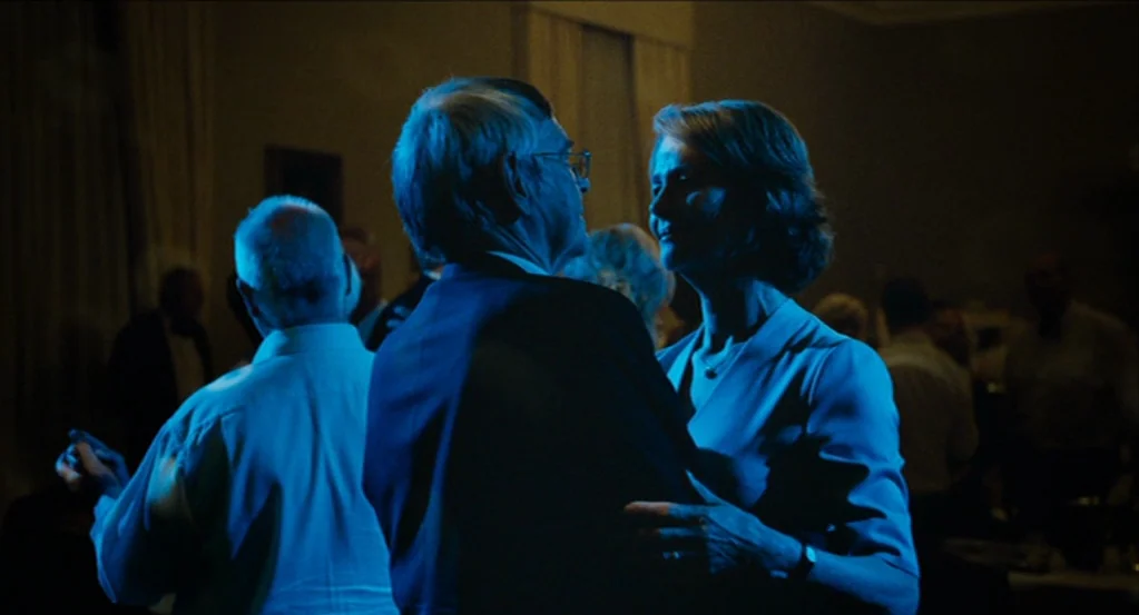 45 Years (2015) movie still: medium — A dimly lit ballroom interior with guests in the background obscured by heavy shadow. An older couple dances…