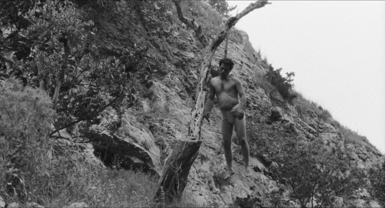 The Gospel According To St. Matthew (1964) movie still: fullbody — A rugged, barren rock formation features sparse vegetation and dry brush along…