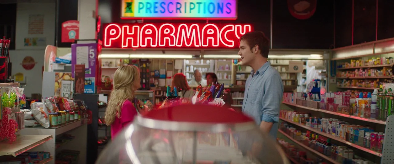 Promising Young Woman (2020) movie still: medium — A cluttered retail space with shelves filled with colorful product packaging and bright neon…