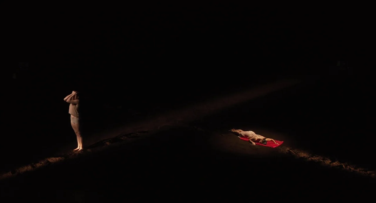 Pina (2011) movie still: wide — A dark, empty landscape features two distinct beams of light hitting the ground. One figure stands upright while…