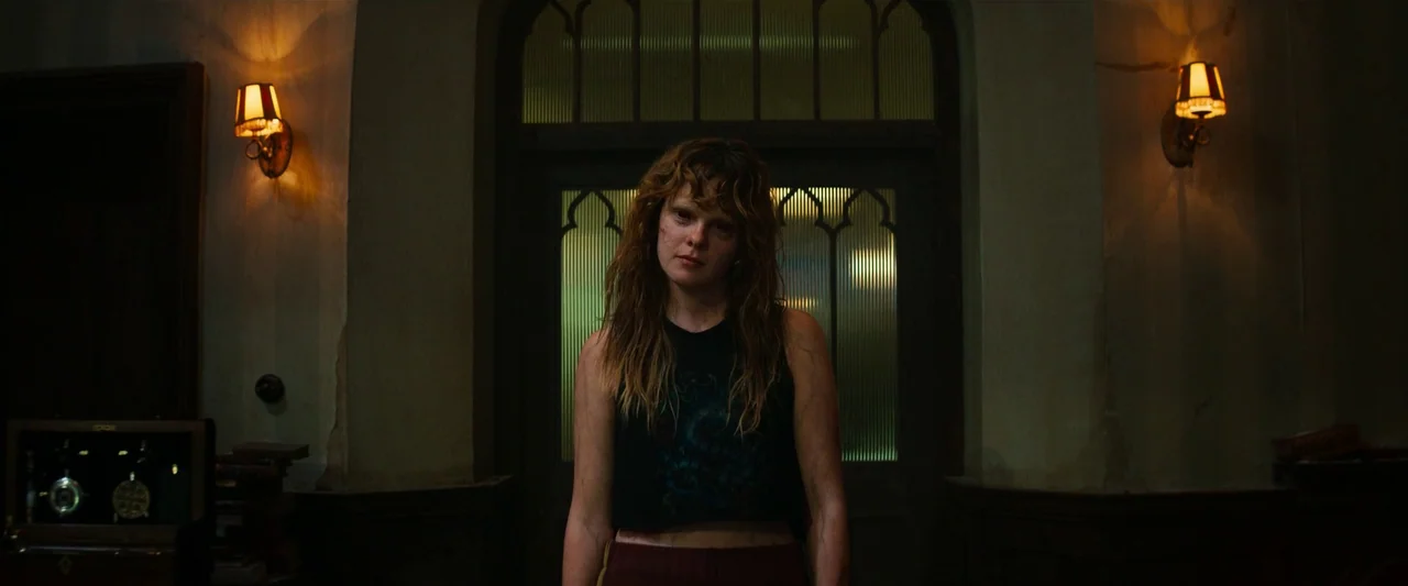 The Pope’s Exorcist (2023) movie still: medium — A dark, dimly lit entrance hall features textured green glass doors and plaster walls. A young…