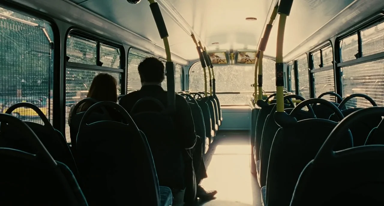 Children Of Men (2006) movie still: medium — The interior of a public transit bus features rows of dark, empty seats. A man and a woman sit…