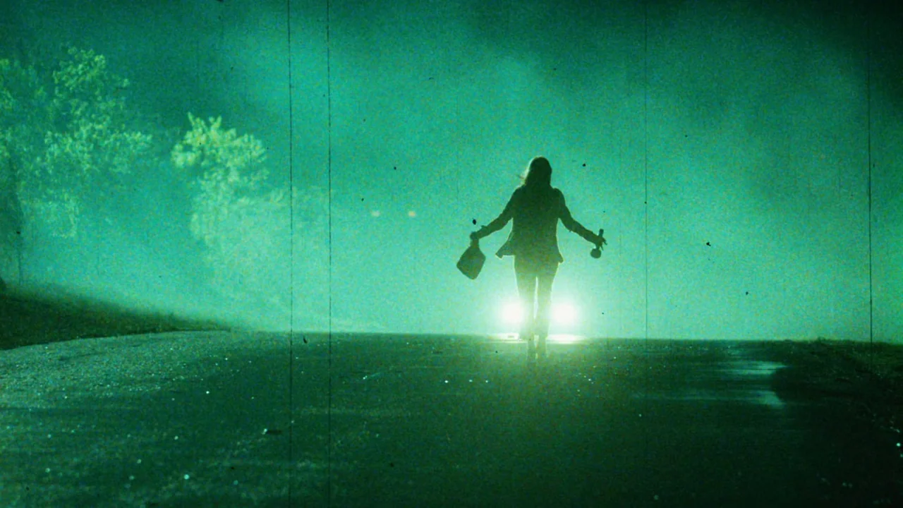 Planet Terror (2007) movie still: wide — A dark, misty road at night is illuminated by bright vehicle headlights. A person walks away into the…