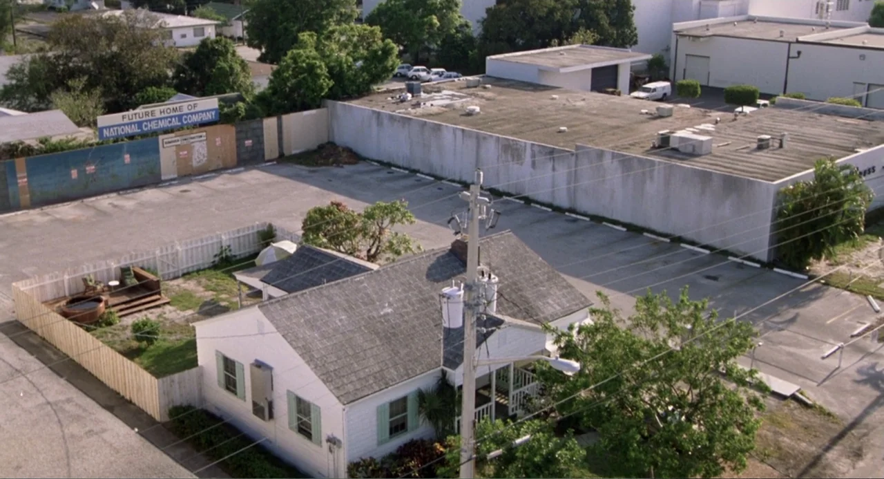 Harry and the Butler (1961) movie still: wide — A single-story white house sits beside a large concrete industrial parking lot area. A wooden fence…