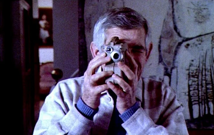Jacquot de Nantes (1991) movie still: closeup — An interior space with a textured painting hanging on the wall behind the subject. An elderly man…