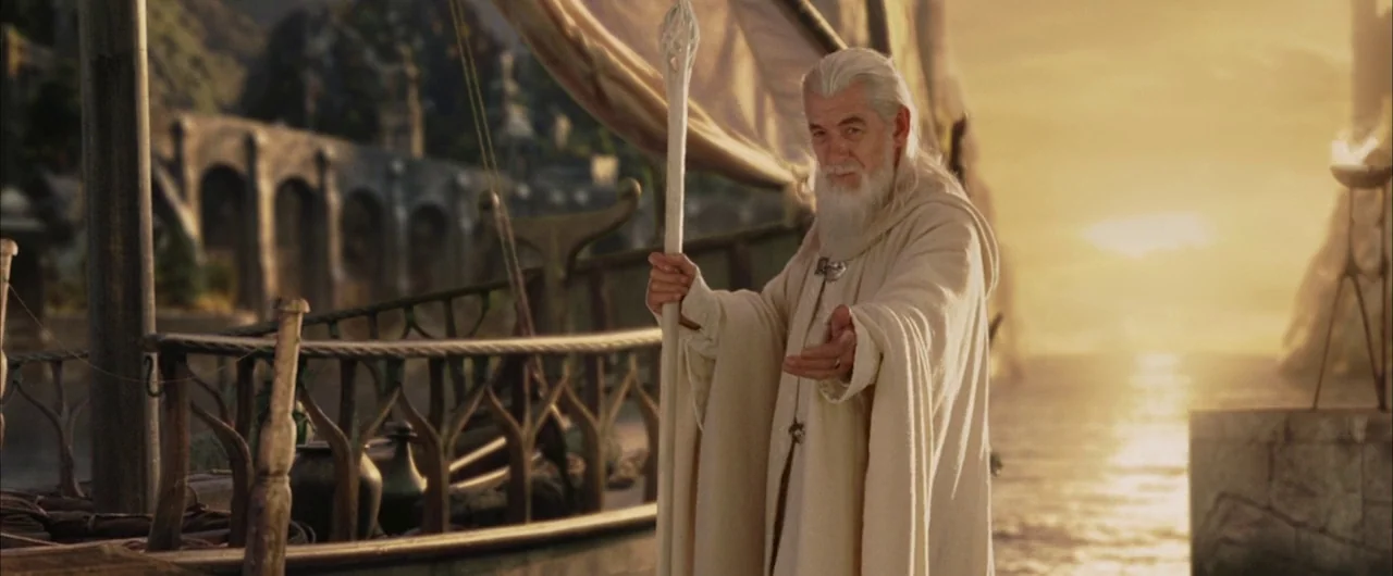 The Lord of The Rings: The Return of the King (2003) movie still: medium — An ornate wooden boat sails near a stone archway during a golden sunset.…