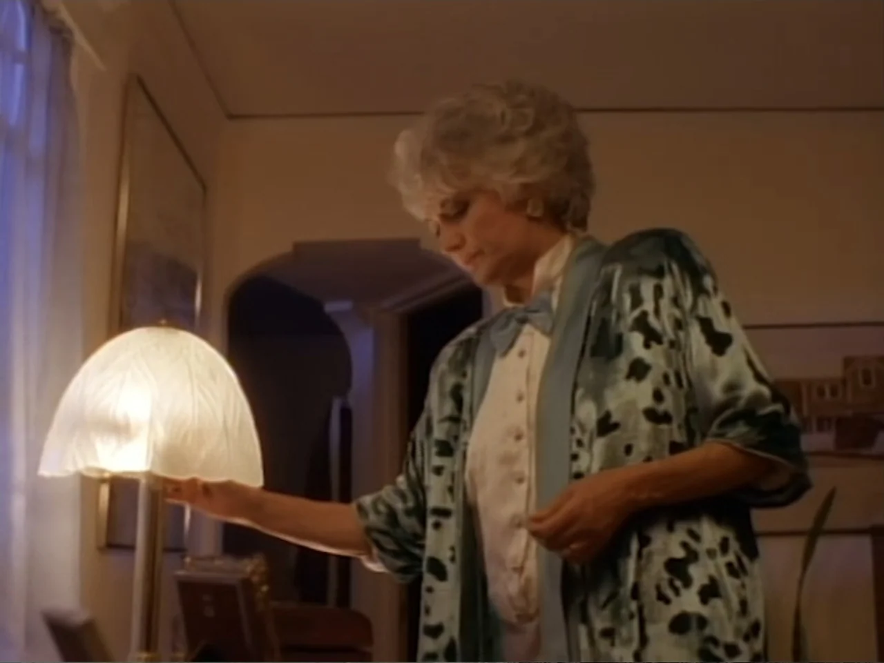 My First Love (1988) movie still: medium — A domestic interior features a table lamp positioned next to a sheer curtained window. A woman in a…