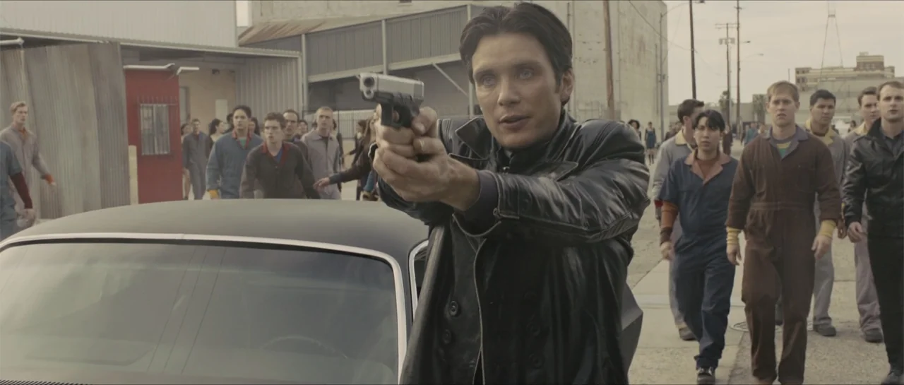 In Time (2011) movie still: medium — An industrial street with a crowd of people walking toward a black car. A man in the foreground stands in front…