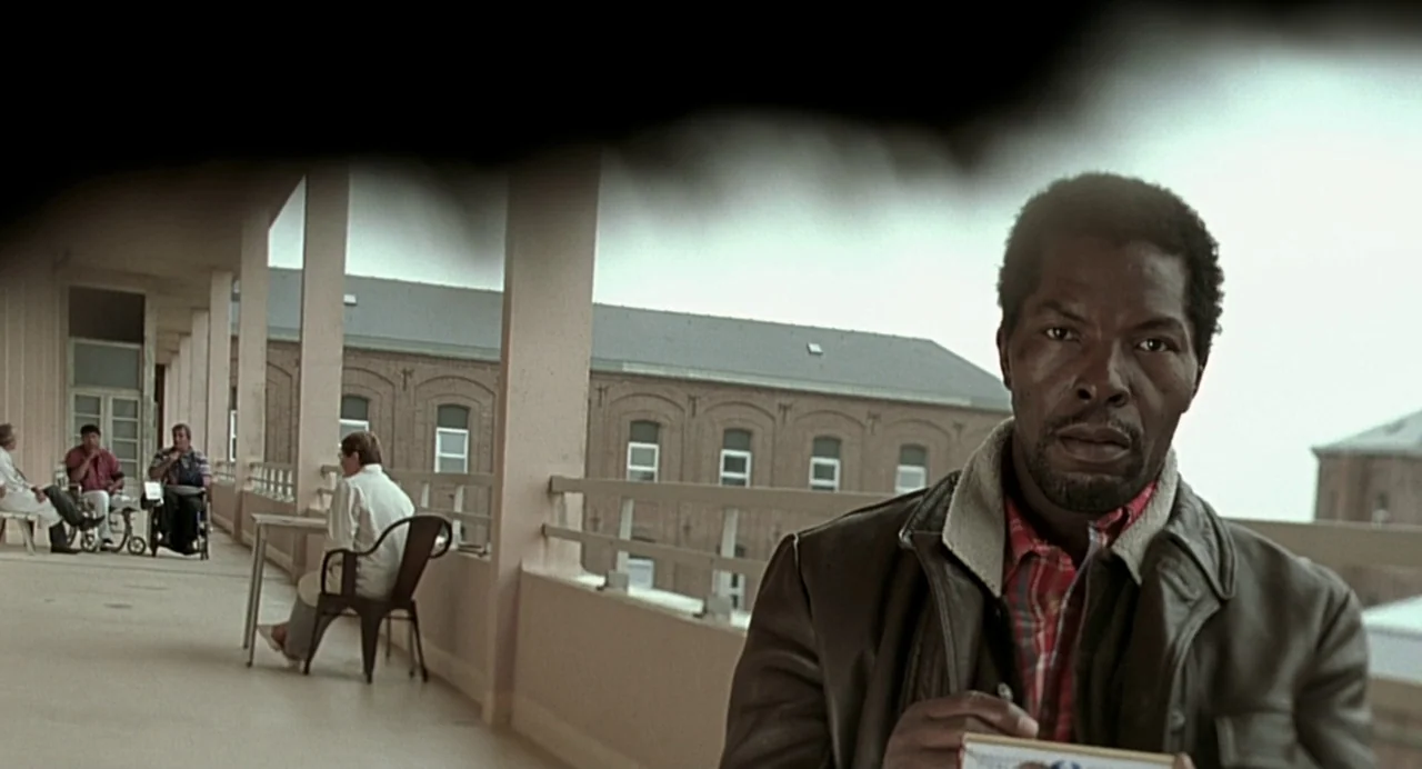 The Diving Bell and the Butterfly (2007) movie still: medium — A long concrete balcony lined with pillars looks out toward a brick hospital…