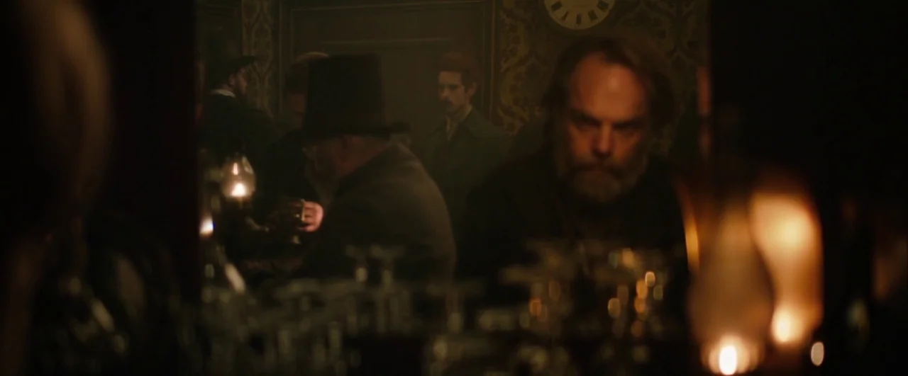 Black ’47 (2018) movie still: medium — A dim, smoky 19th-century pub features patterned wallpaper and an analog clock on the wall. A bearded man…