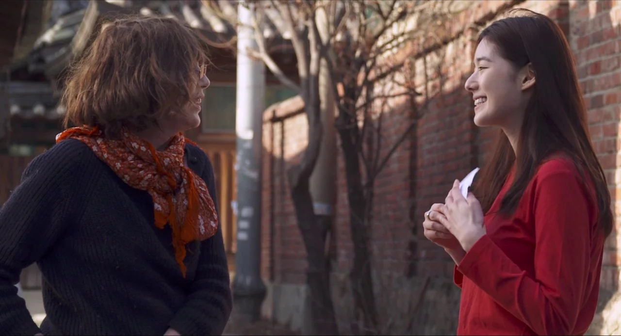 Nobody’s Daughter Haewon (2013) movie still: medium — A narrow outdoor walkway features red brick walls and bare trees. Two women stand opposite…