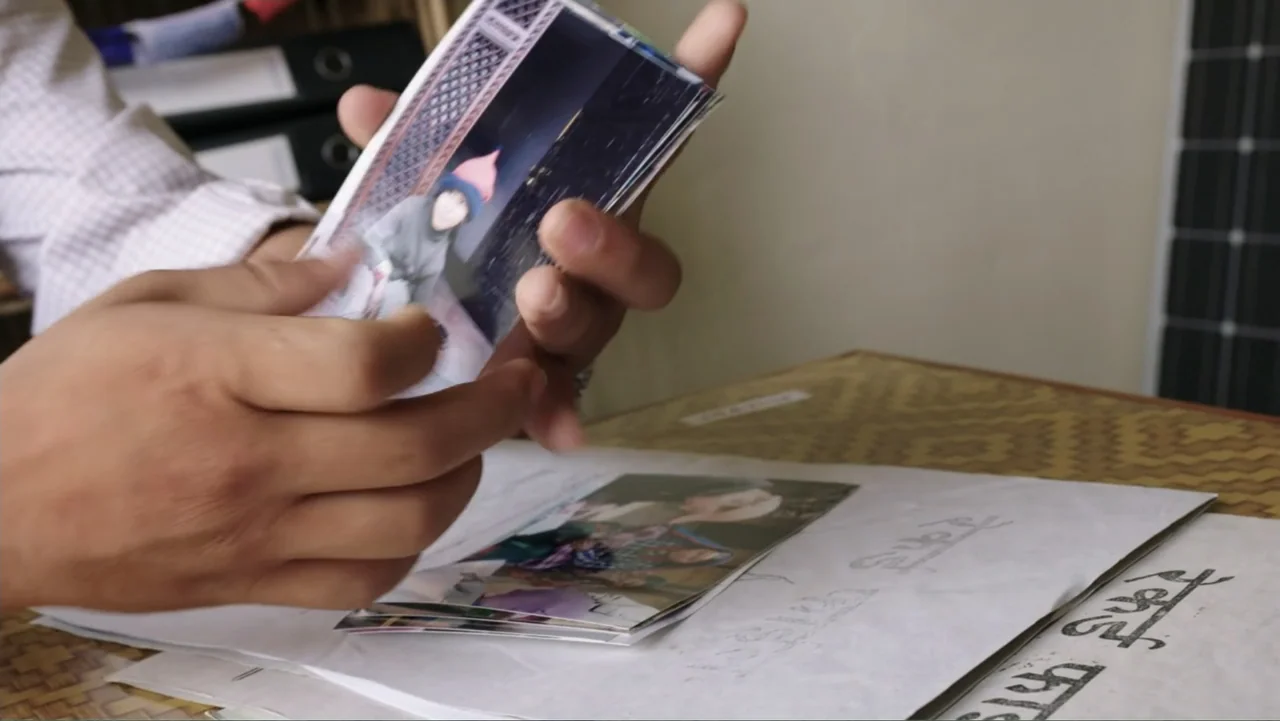 Finding the Way Home (1991) movie still: closeup — A person holds a small printed photograph while sitting at a desk with papers. The focus remains…