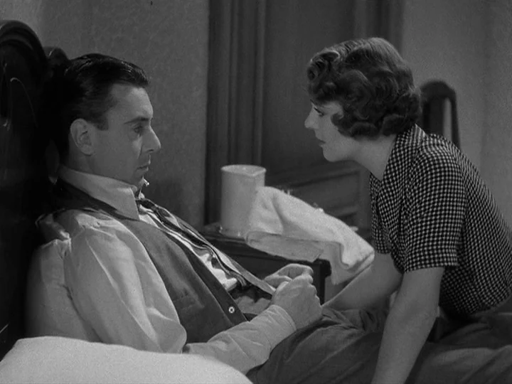 42nd Street (1933) movie still: medium — A dark bedroom with a person resting in bed against a wooden headboard. A second person kneels beside the…