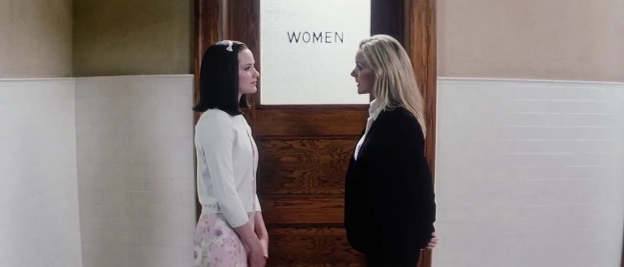 Pretty Persuasion (2005) movie still: medium — A public restroom features white tile walls and a central wooden door marked WOMEN. A younger girl…