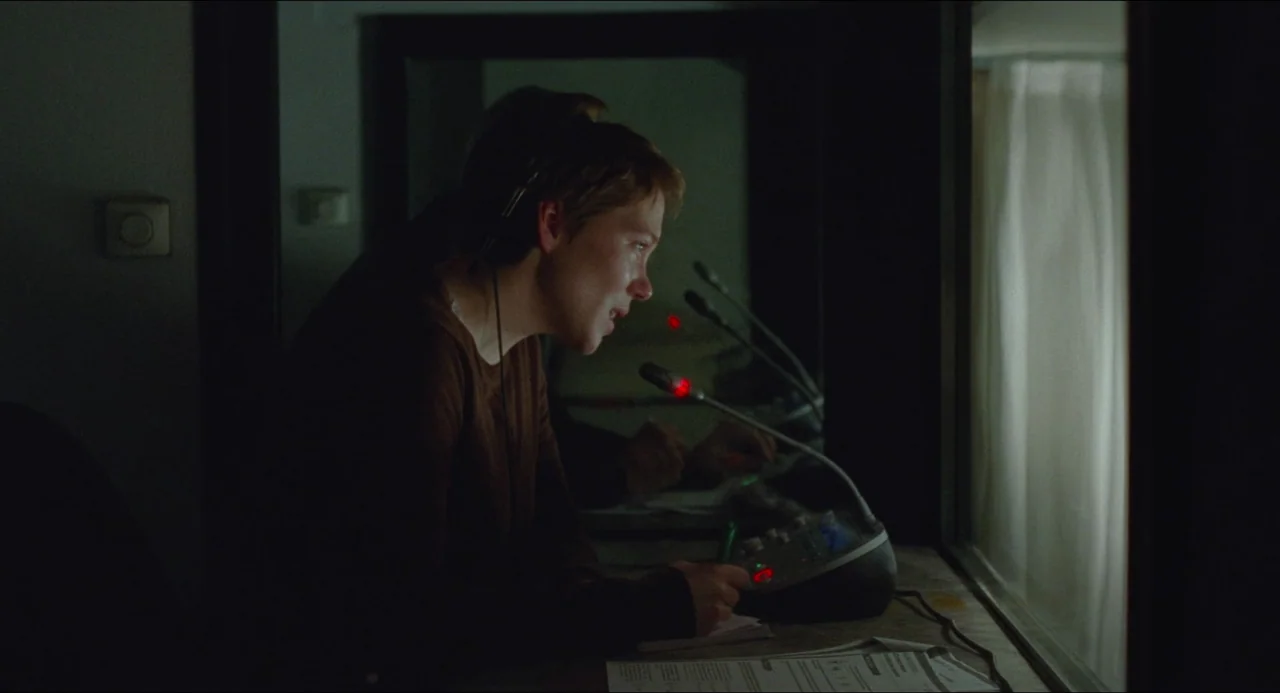 One Fine Morning (2022) movie still: medium — A dark, cramped translation booth features a console with multiple microphones and sound equipment. A…