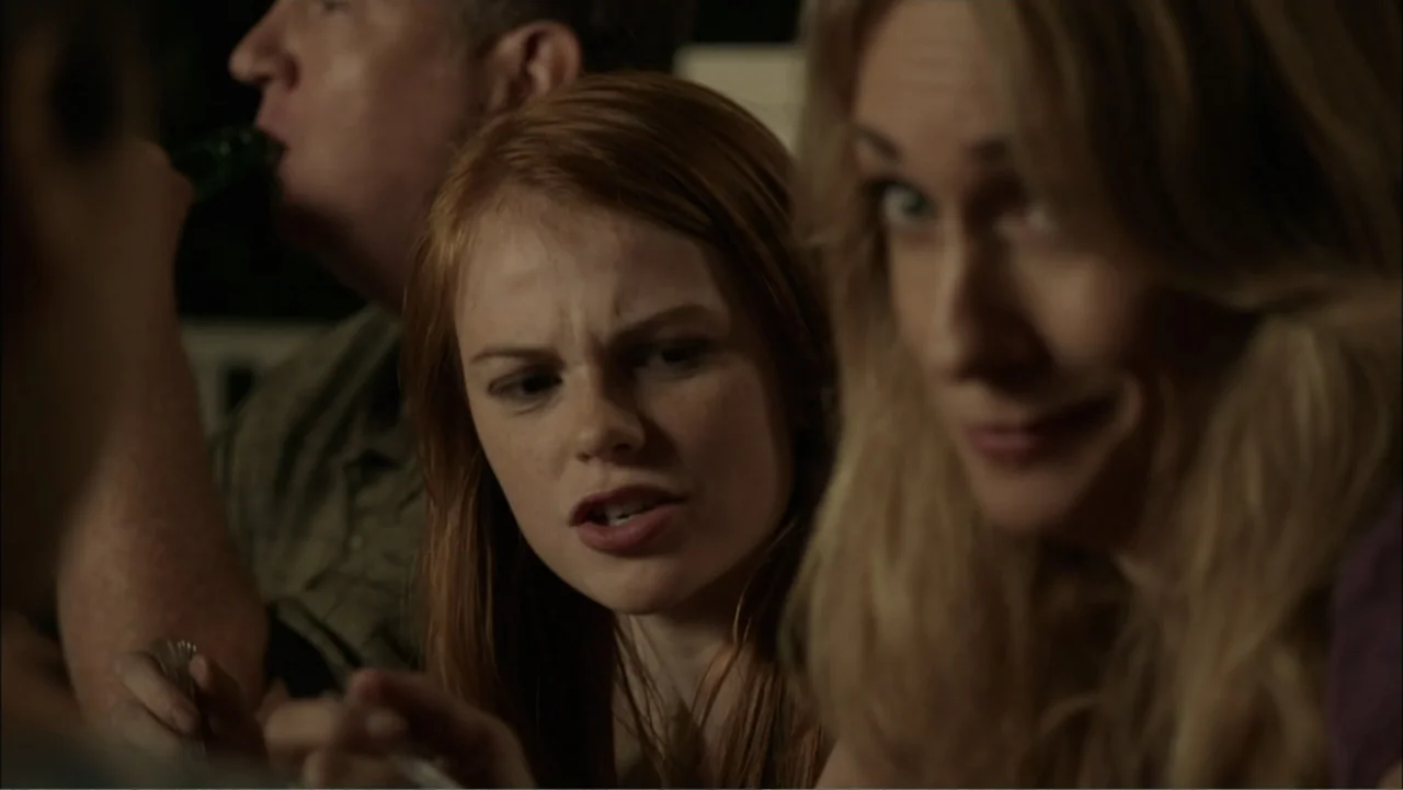 Dark Skies (2013) movie still: medium — A dimly lit room holds three people gathered closely around a table at night. A young woman in the center…