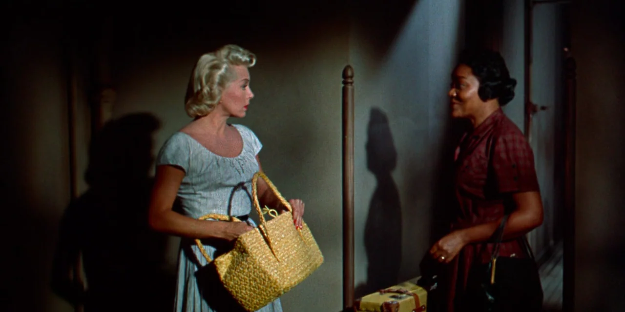 Imitation of Life (1959) movie still: medium — A dimly lit narrow hallway with a wooden post and shadowed walls. Two women stand facing one another…