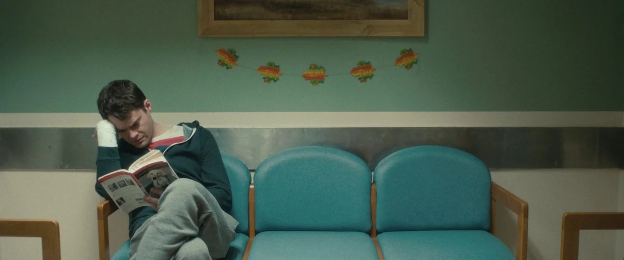 The Skeleton Twins (2014) movie still: medium — A waiting room features teal walls decorated with a festive paper leaf banner. A man sits in a row…