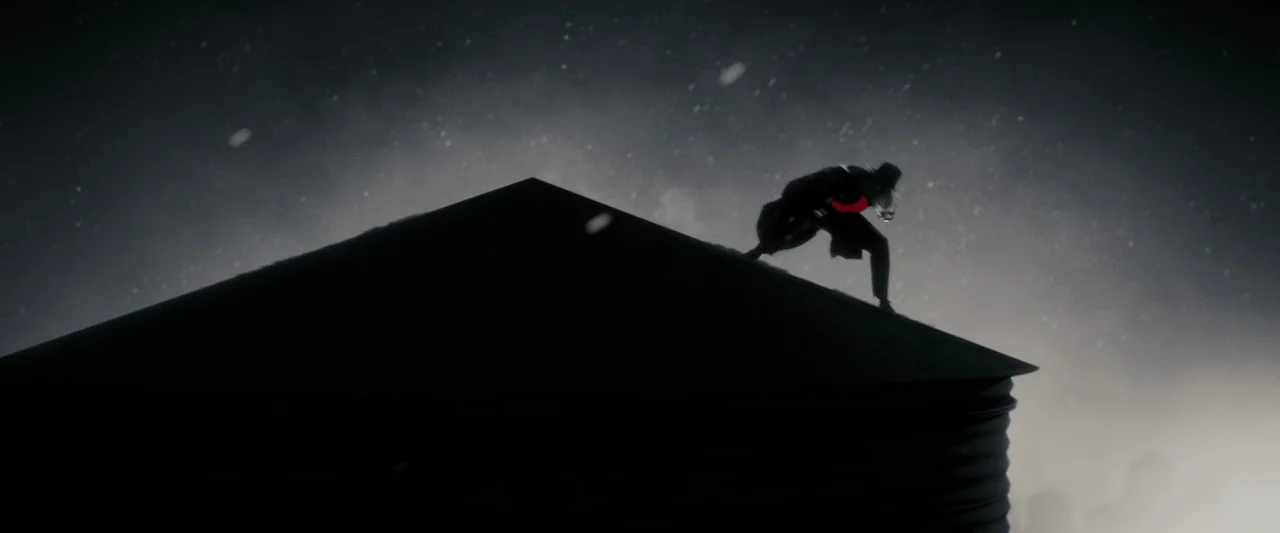 The Spirit (2008) movie still: wide — A dark, textured metal structure stands against a night sky filled with falling snow. A figure in a dark coat…