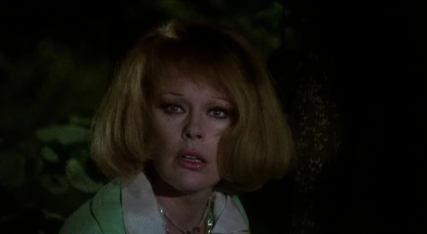 Lisa and The Devil (1973) movie still: closeup — A woman stands in a dark wooded area at night. She looks toward the side of the frame with a…