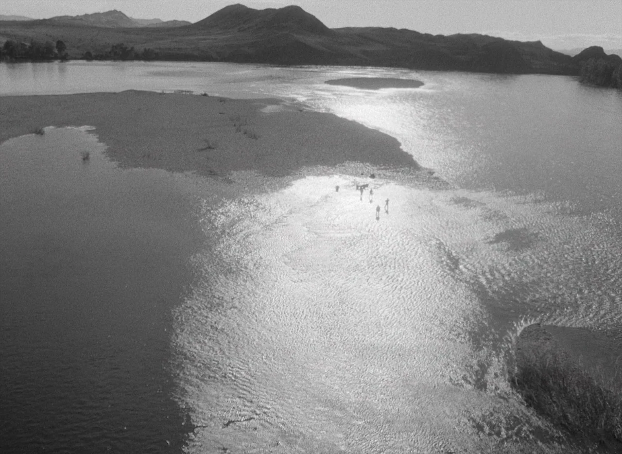 Letter Never Sent (1960) movie still: wide — A wide aerial view shows a sprawling river with a sandbar island in the middle. Small figures traverse…