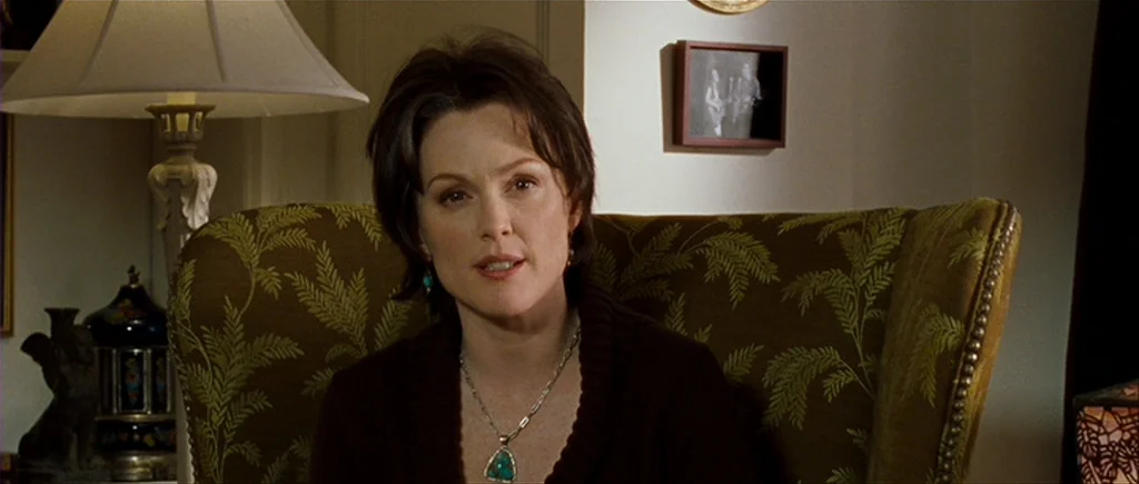 I’m Not There (2007) movie still: medium — A woman sits in a green patterned armchair inside a residential room. She is positioned in front of a…