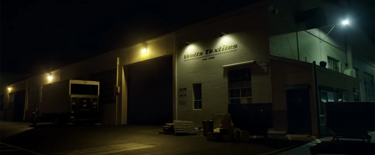 Lights Out (2016) movie still: establishing — The exterior wall of a commercial textile building features a large sign under security lighting. A…