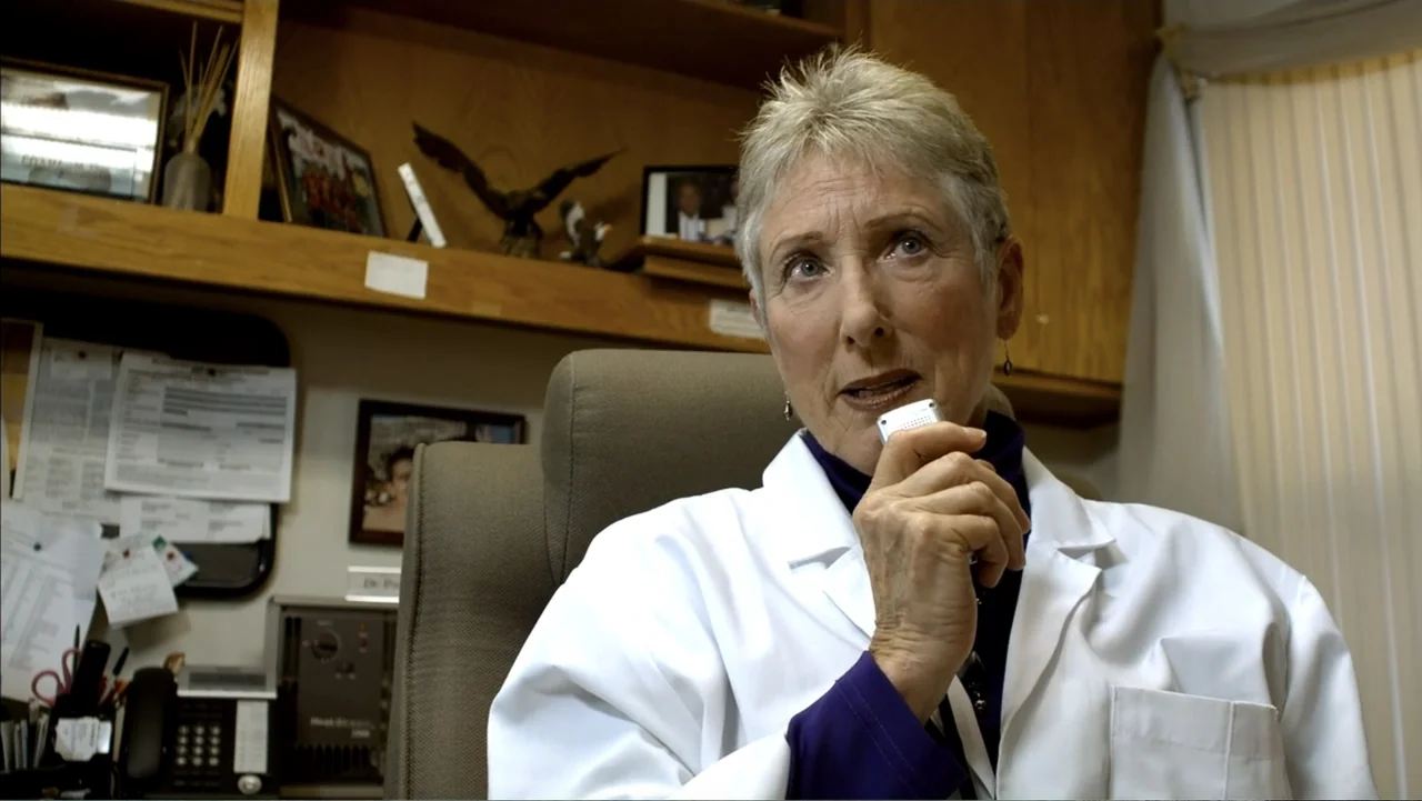 Abandoned Dead (2015) movie still: medium — A cluttered doctor's office contains wooden shelving units holding framed photographs and memorabilia. A…