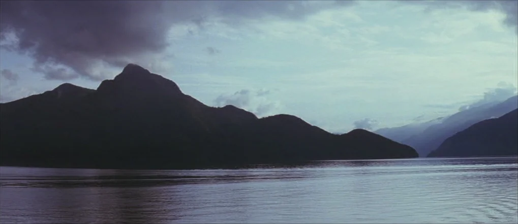 Insomnia (2002) movie still: establishing — A wide view of a large body of water bordered by silhouettes of mountain ranges. Overcast, cloudy sky…