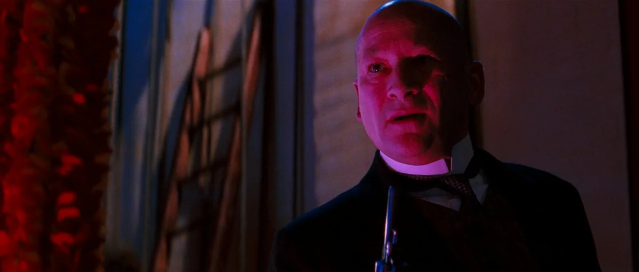 Moulin Rouge! (2001) movie still: medium — A dimly lit passenger train car interior with dark textures and wood paneling visible. A middle-aged man…