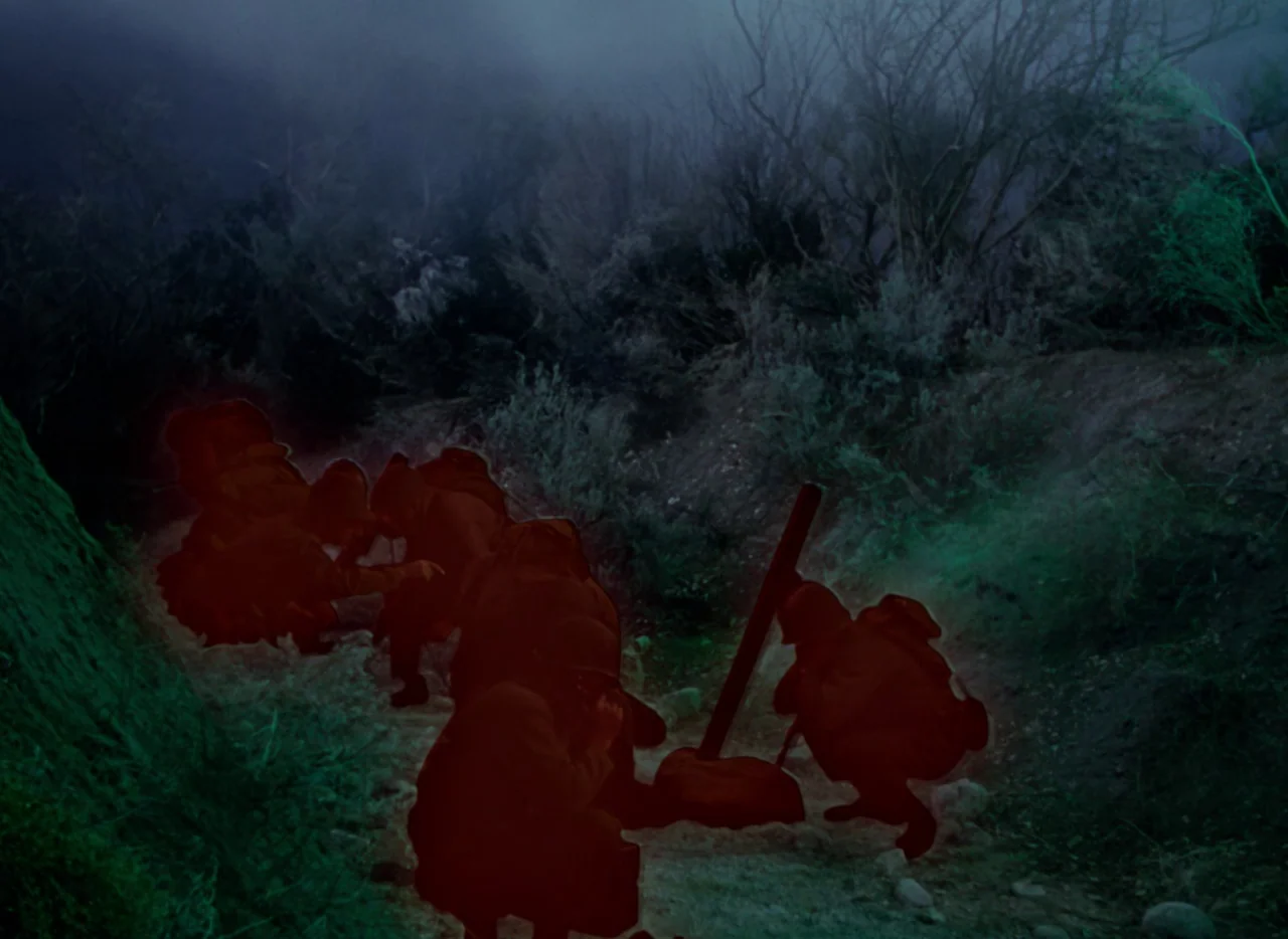 The War of the Worlds (1953) movie still: wide — A group of soldiers in helmets crouch in a dirt trench at night. Greenish blue lighting covers the…