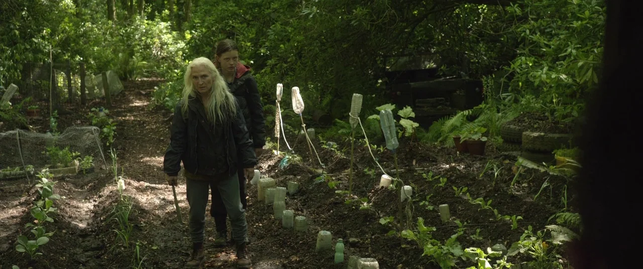 The Survivalist (2015) movie still: medium — A rural vegetable garden with raised soil beds features numerous inverted plastic bottles on stakes.…