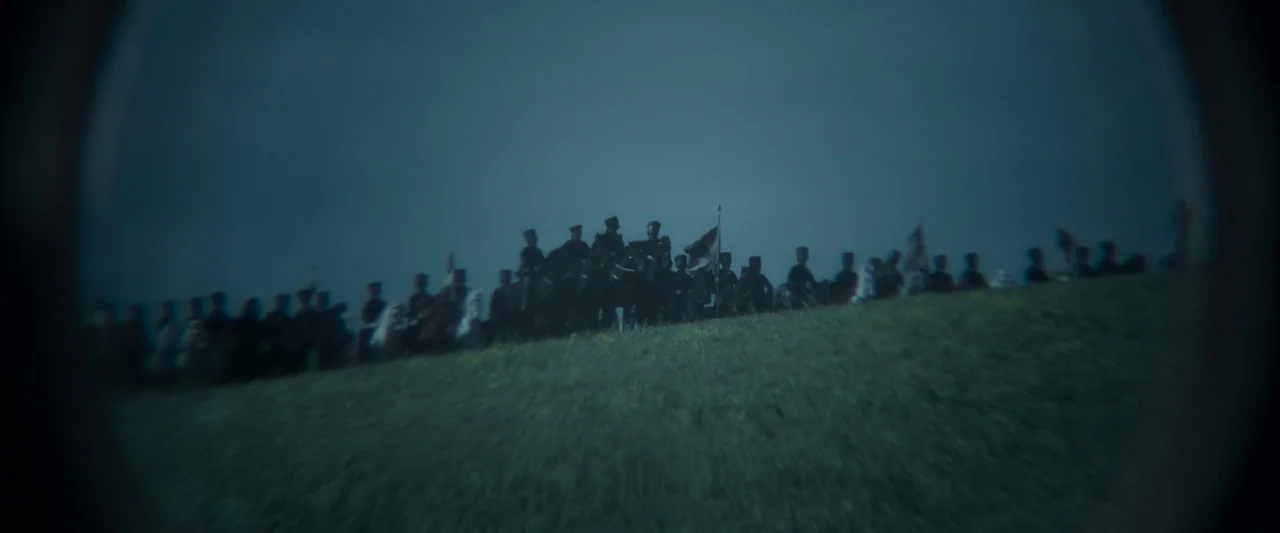 Napoleon (2023) movie still: wide — A line of soldiers on horseback silhouettes against a dark blue evening sky. The riders move along the crest of…