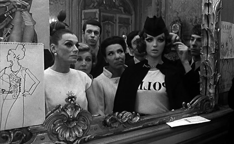 Who Are You, Polly Maggoo? (1966) movie still: medium — A crowded fashion atelier contains ornate mirrors and sketches of clothing designs on walls.…