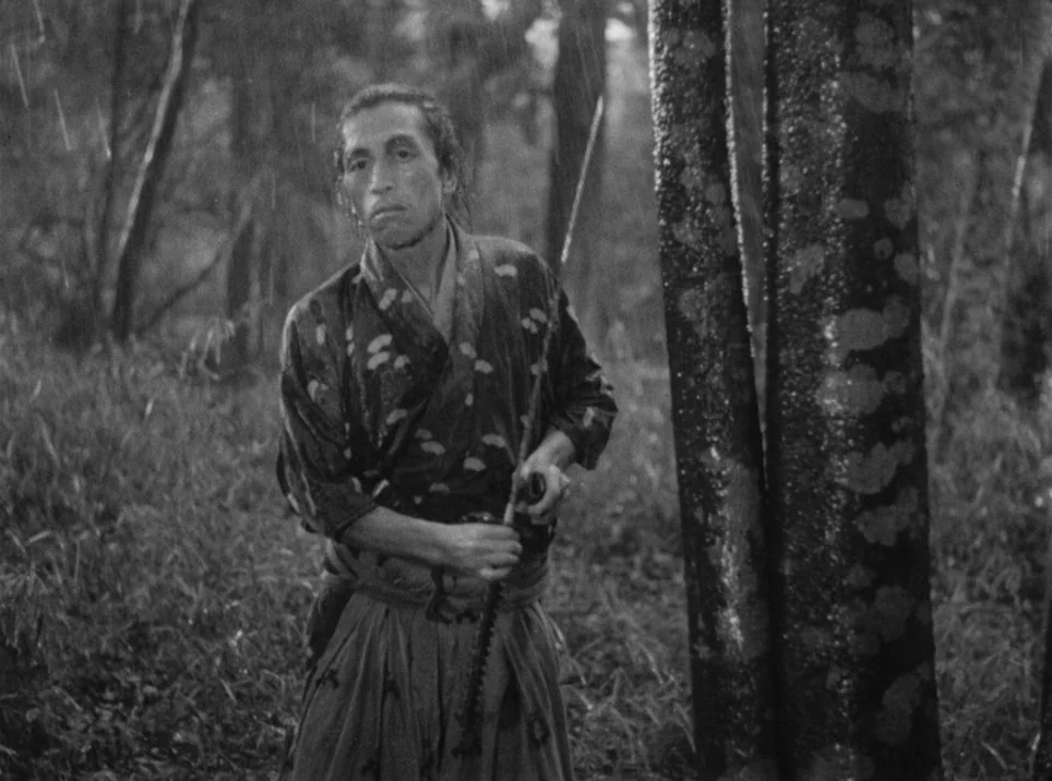 Seven Samurai (1954) movie still: medium — A dense bamboo grove at daytime during a heavy rainstorm. A man in traditional samurai clothing stands…