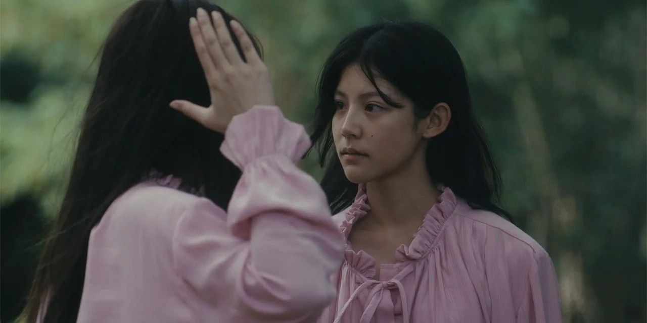 Host (2020) movie still: medium — A green woodland setting provides the backdrop for two young women in matching outfits. One woman reaches forward…